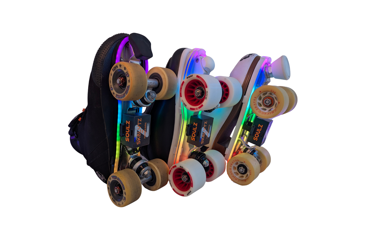 Three quad roller skates in a row, side-on, with rainbow LED light strips and SK8Lytz SOULZ units under the soles